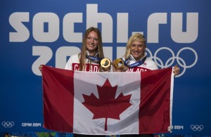 Kaillie Humphries, right, and Heather Moyse, bobsleigh gold medalists, pose with the Canadian flag as they are introduced as the flag bearers for the closing ceremonies at the Sochi Winter Olympics Sunday, February 23, 2021 in Sochi. THE CANADIAN PRESS/Paul Chiasson 